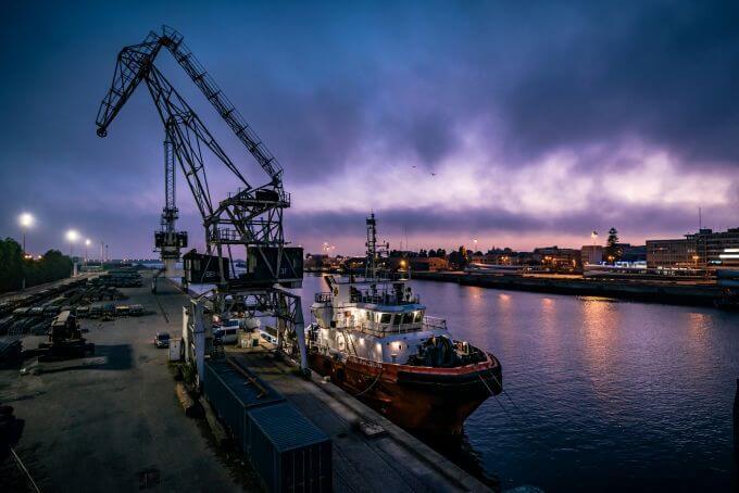 A docked cargo ship with an industrial crane in the background at dusk, representing the need for strong maritime network connectivity.